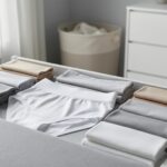 Folded seamless boyshorts and high-waist briefs arranged neatly on a light fabric surface in a bright, minimalist bedroom setting.