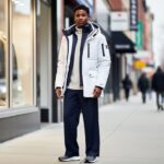 Model wearing a layered insulated Canadian parka and streetwear in an urban setting with softly blurred winter city elements.